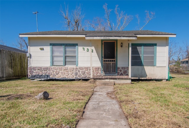 view of front of house with stone siding, fence, and a front yard