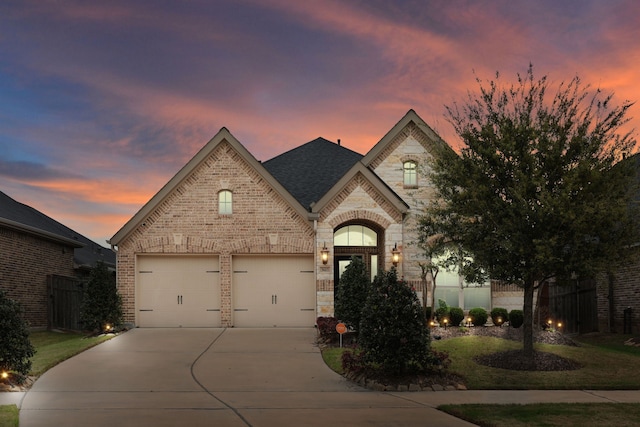 french country inspired facade featuring brick siding, a shingled roof, fence, concrete driveway, and stone siding