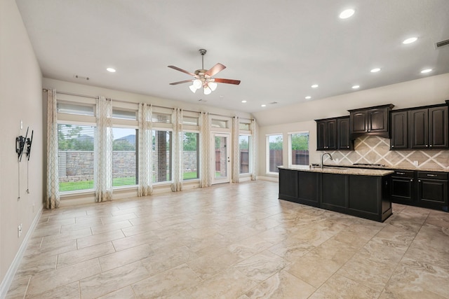 kitchen with a sink, a ceiling fan, gas stovetop, decorative backsplash, and a center island with sink