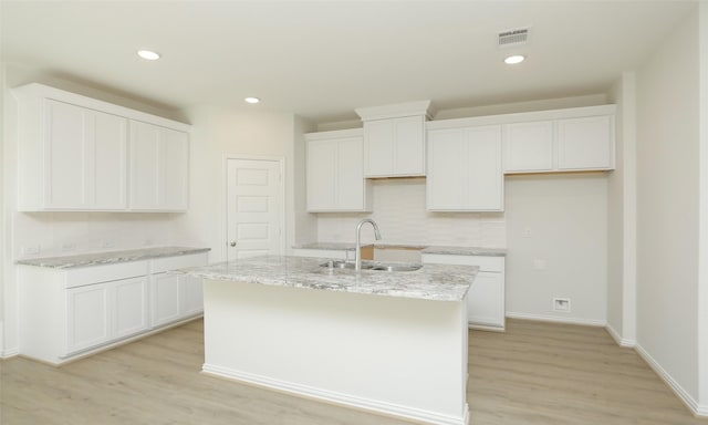 kitchen featuring light wood finished floors, white cabinetry, a kitchen island with sink, and visible vents