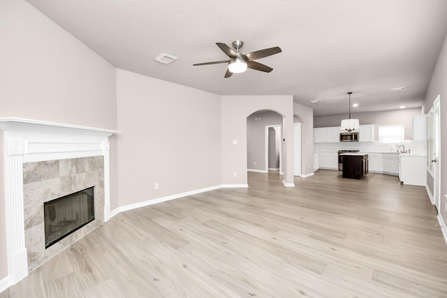 unfurnished living room featuring visible vents, arched walkways, a tiled fireplace, light wood-style flooring, and ceiling fan