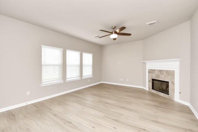 unfurnished living room with ceiling fan, a tile fireplace, visible vents, baseboards, and light wood-type flooring