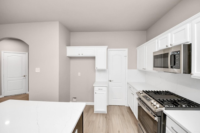 kitchen with stainless steel appliances, light wood finished floors, light stone counters, and white cabinets