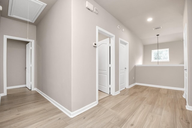 hall featuring attic access, light wood-type flooring, visible vents, and baseboards