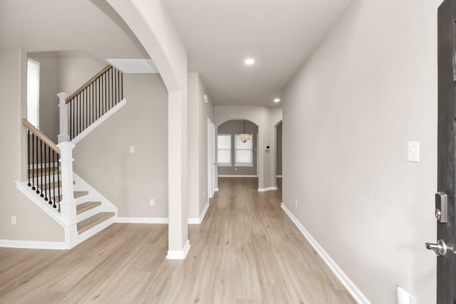 foyer with arched walkways, stairs, light wood-style flooring, and baseboards