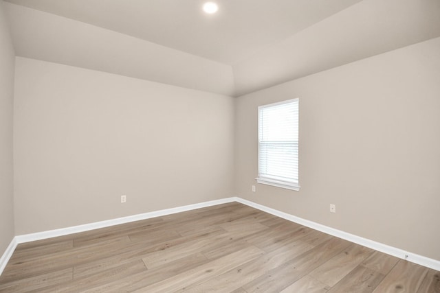 spare room with lofted ceiling, light wood-style flooring, and baseboards