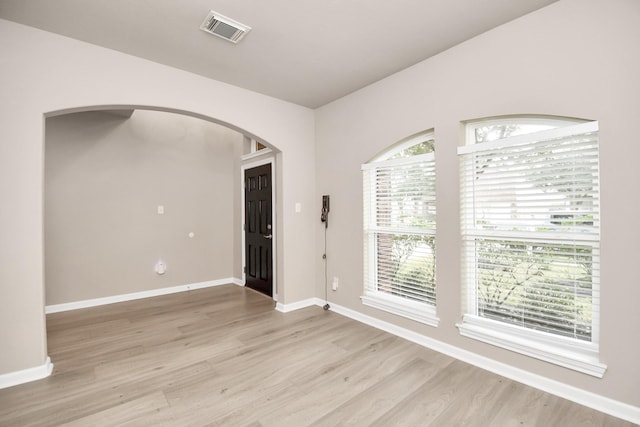 spare room with light wood finished floors, baseboards, visible vents, and arched walkways