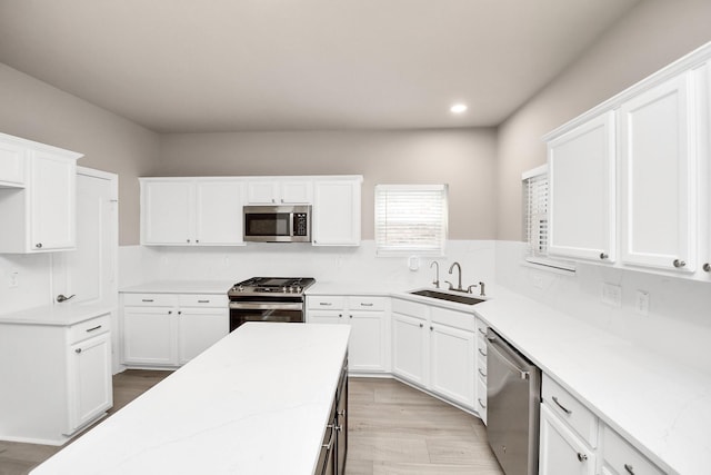 kitchen with light stone counters, a sink, white cabinets, appliances with stainless steel finishes, and light wood-type flooring