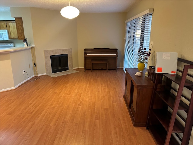 living room featuring light wood-style flooring, baseboards, and a tiled fireplace