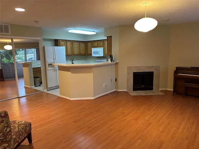 kitchen featuring light wood-style flooring, white appliances, visible vents, light countertops, and a tiled fireplace