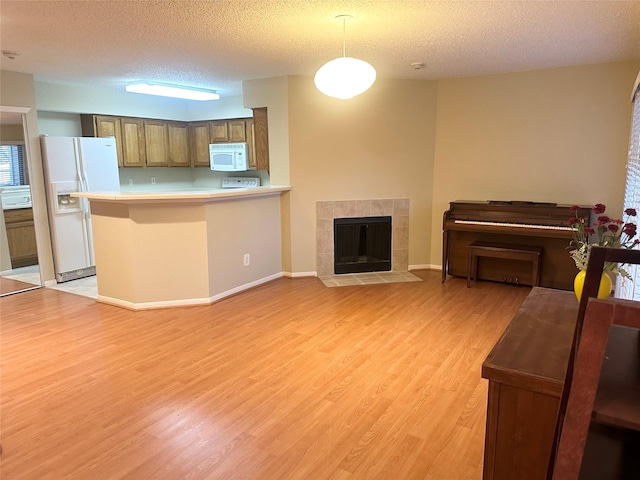 kitchen featuring light countertops, a tiled fireplace, light wood-type flooring, white appliances, and a peninsula