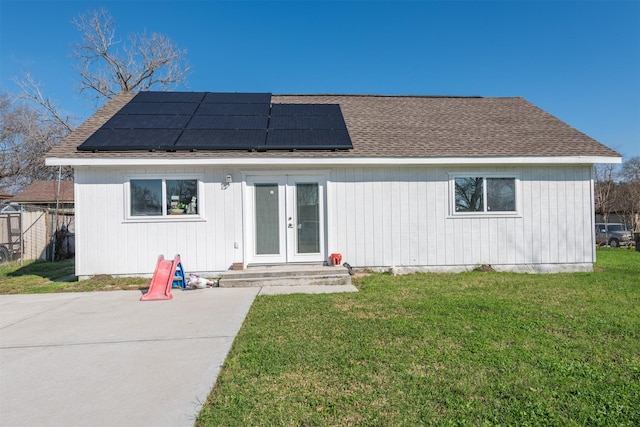 view of front of property with a shingled roof, fence, french doors, roof mounted solar panels, and a front yard