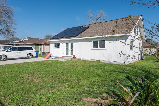 view of front of property featuring french doors, a front lawn, a shingled roof, and roof mounted solar panels