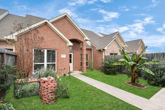 view of front of house featuring brick siding, roof with shingles, a front yard, and fence