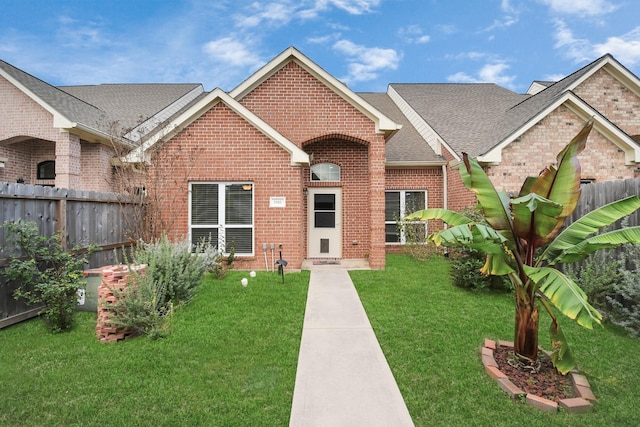 view of front of house with roof with shingles, brick siding, a front lawn, and fence