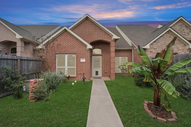 ranch-style house featuring a yard, brick siding, a shingled roof, and fence