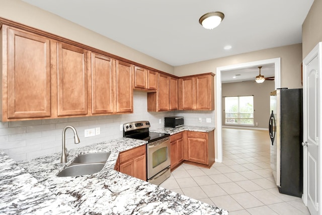 kitchen with light stone counters, backsplash, appliances with stainless steel finishes, light tile patterned flooring, and a sink