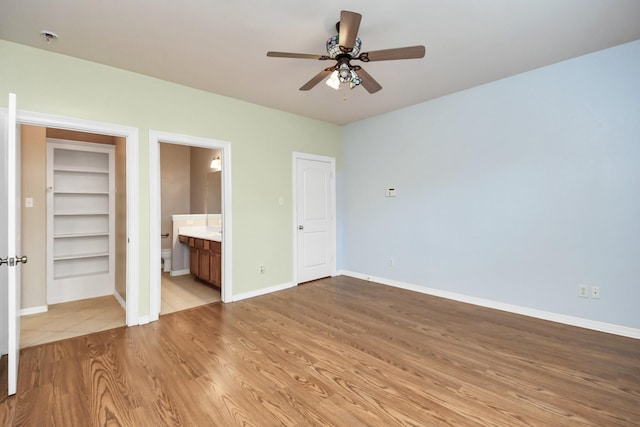 unfurnished bedroom featuring ensuite bathroom, wood finished floors, a ceiling fan, and baseboards