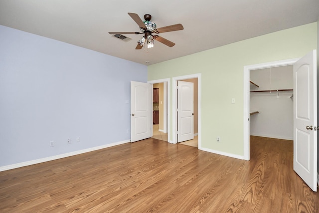 unfurnished bedroom featuring wood finished floors, a ceiling fan, visible vents, baseboards, and a spacious closet