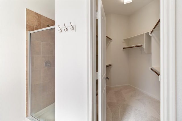 full bathroom with a shower stall, a walk in closet, and baseboards