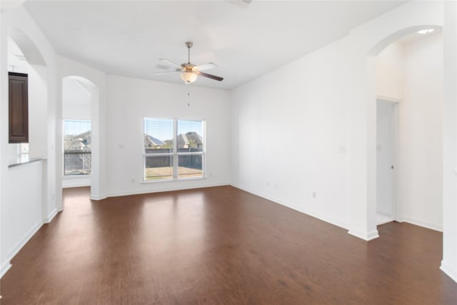 spare room with ceiling fan, arched walkways, dark wood finished floors, and baseboards