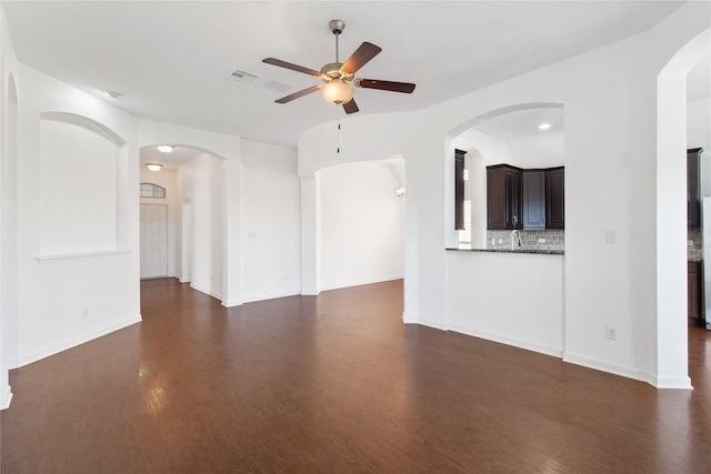 unfurnished living room with a ceiling fan, dark wood-style flooring, a sink, and baseboards