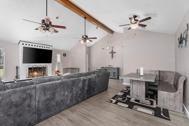 living area featuring a warm lit fireplace, lofted ceiling with beams, baseboards, and wood finished floors