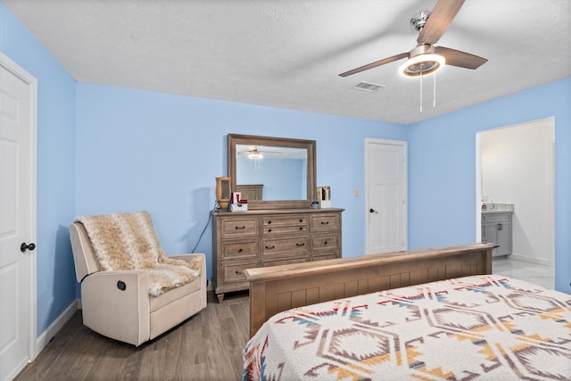 bedroom with a textured ceiling, connected bathroom, wood finished floors, visible vents, and baseboards