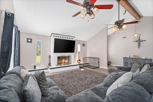 living area featuring baseboards, visible vents, wood finished floors, a lit fireplace, and beam ceiling