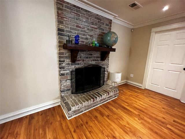 unfurnished living room featuring crown molding, visible vents, a brick fireplace, wood finished floors, and baseboards