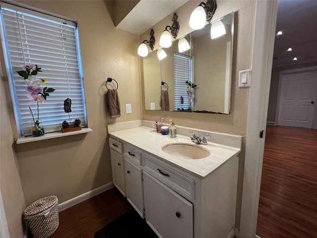 bathroom with a textured wall, vanity, baseboards, and wood finished floors