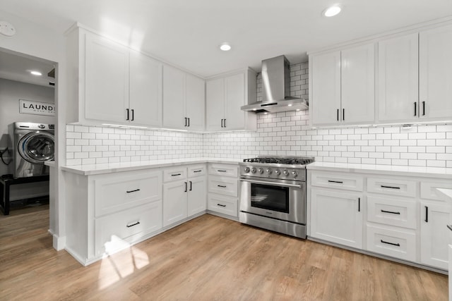 kitchen with light wood finished floors, light countertops, washer / dryer, high end stove, and wall chimney exhaust hood