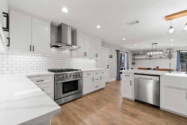 kitchen featuring wall chimney exhaust hood, appliances with stainless steel finishes, light wood-style floors, and white cabinets