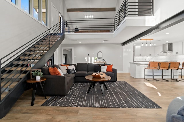 living room featuring beam ceiling, a notable chandelier, a towering ceiling, light wood-type flooring, and stairs