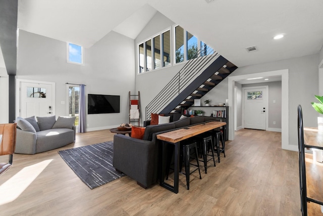 living room with baseboards, visible vents, stairs, a high ceiling, and light wood-type flooring