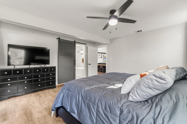 bedroom featuring a barn door, visible vents, light wood-style flooring, and a ceiling fan