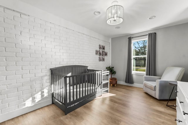 bedroom featuring baseboards, brick wall, wood finished floors, a fireplace, and a chandelier