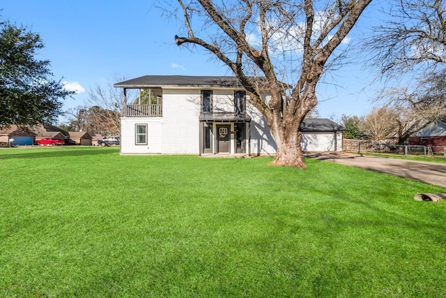 view of front facade with a balcony, brick siding, fence, driveway, and a front yard