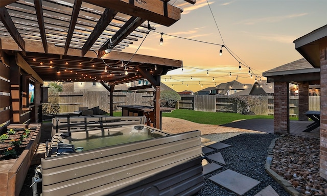 deck at dusk with an outdoor hot tub, a patio, a fenced backyard, a yard, and a pergola