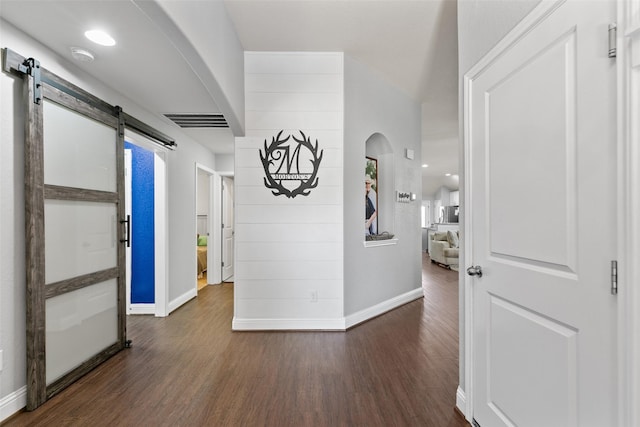 corridor featuring a barn door, wood finished floors, visible vents, and baseboards