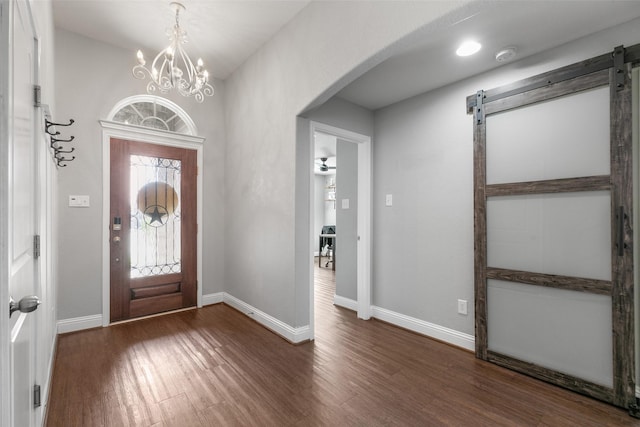 entryway with arched walkways, a notable chandelier, a barn door, wood finished floors, and baseboards