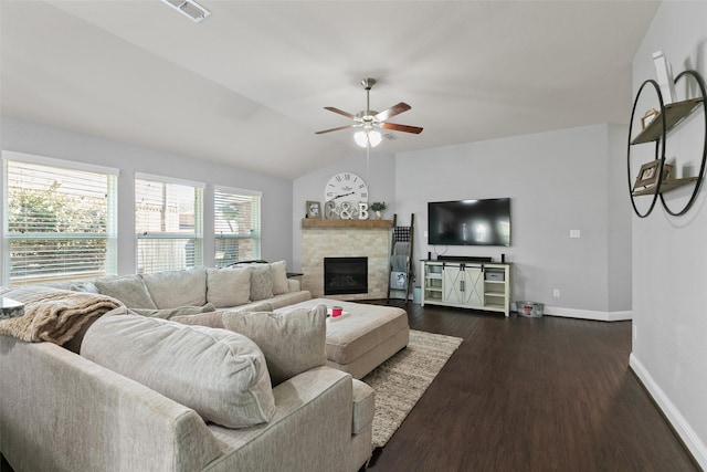 living room featuring lofted ceiling, ceiling fan, a stone fireplace, dark wood-type flooring, and baseboards