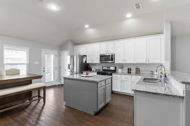 kitchen featuring stainless steel appliances, a sink, white cabinets, vaulted ceiling, and light stone countertops