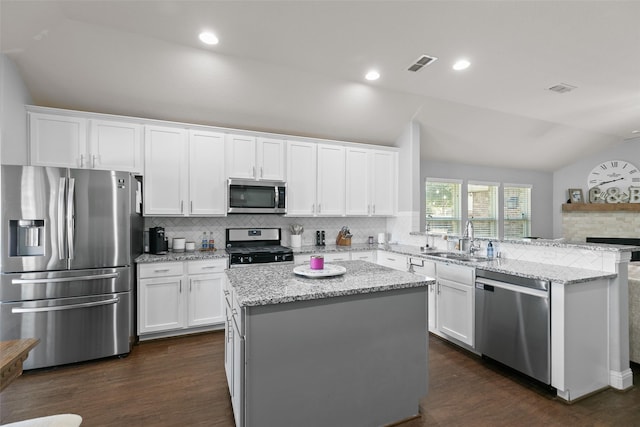 kitchen with stainless steel appliances, lofted ceiling, white cabinets, a sink, and a peninsula