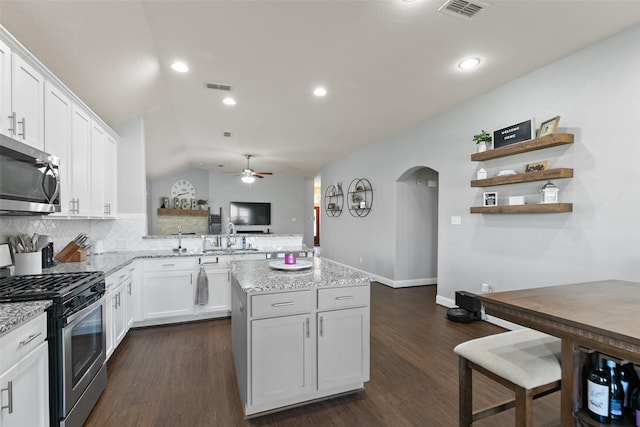 kitchen with visible vents, arched walkways, lofted ceiling, a kitchen island, and appliances with stainless steel finishes