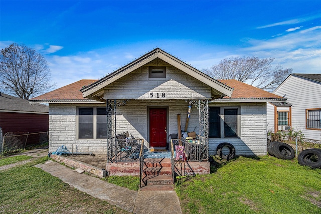 view of front of home with stone siding, a front yard, covered porch, and fence