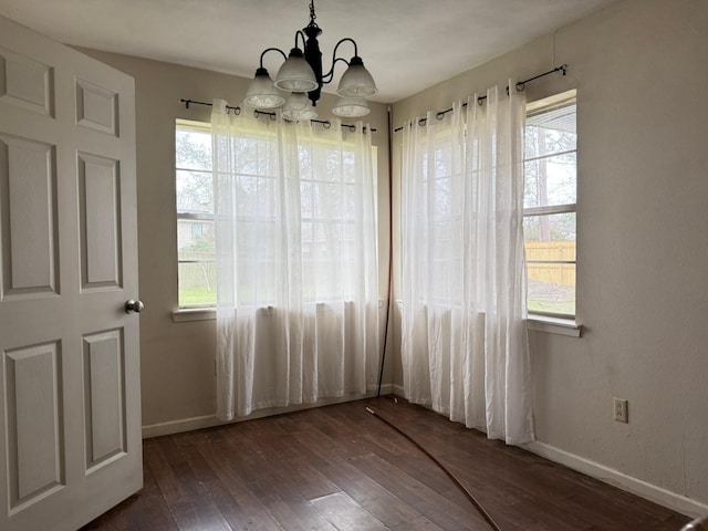 unfurnished dining area with baseboards, a chandelier, and dark wood-type flooring