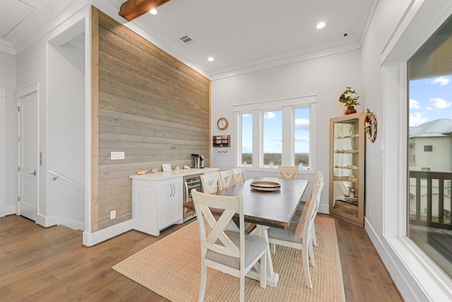 dining room featuring beverage cooler, wood walls, wood finished floors, baseboards, and crown molding