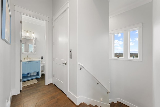 corridor with dark wood-type flooring, baseboards, a sink, and an upstairs landing