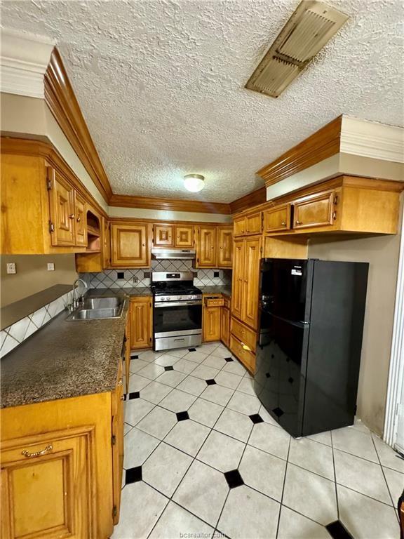 kitchen featuring ornamental molding, freestanding refrigerator, a sink, stainless steel gas range, and under cabinet range hood